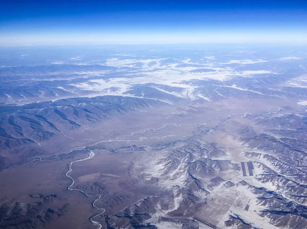 An aerial view of Chinese mountains from the airplane flying high above the ground. A look from the planes window.