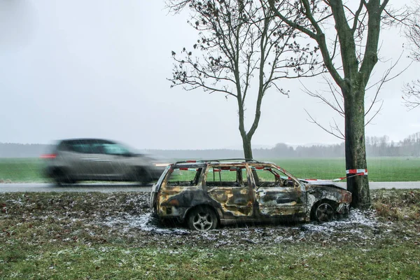 Car destroyed during the traffic accident. It was caused by the bad weather conditions in winter, because of the black ice or snow. The car is burnt, abandoned and stands by the road in the snowfall.