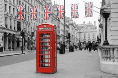 A traditional British red telephone box is standing on the street. Six British flags are hanging above it.  Booth and flags isolated in a black and white picture.  clipart