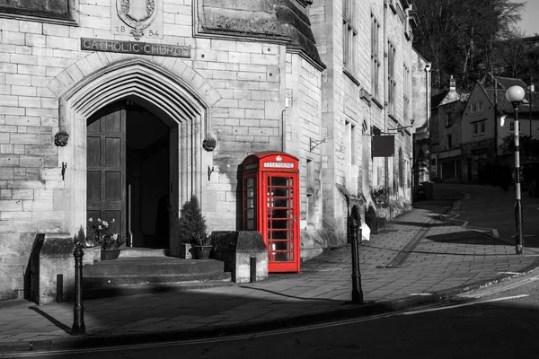 A traditional red British phone box is standing on the street of Bradford on Avon. The booth is isolated in a black and white picture.