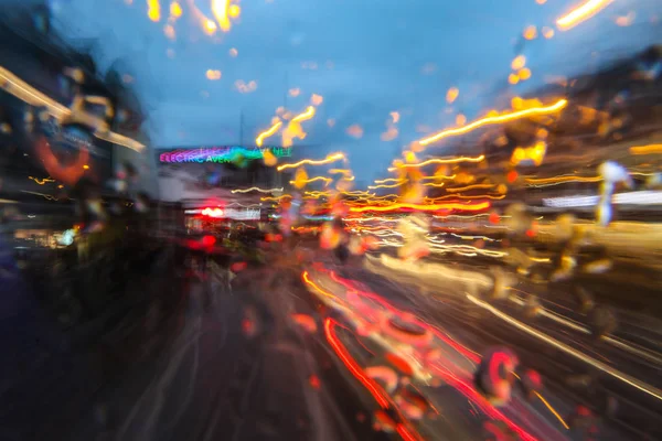 A picture from the driving bus in the evening city during the rain. Everything is abstractly blurred in traces colors.