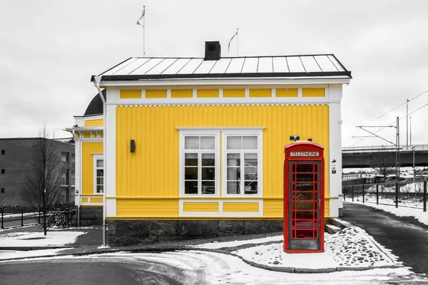 A traditional red British phone box standing by the traditional yellow wooden cottage in Sweden. Unusual couple of country symbols.