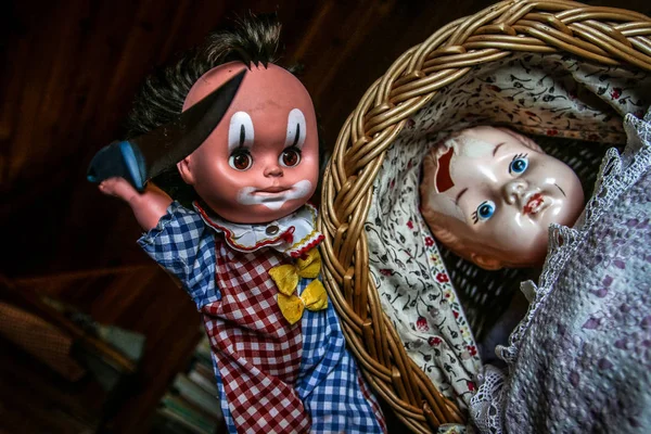 The unused old doll with a hole in its head is lying in the baby carriage and looking quite scary and depressive. The second doll is holding the knife above it. Looks like doll murder.