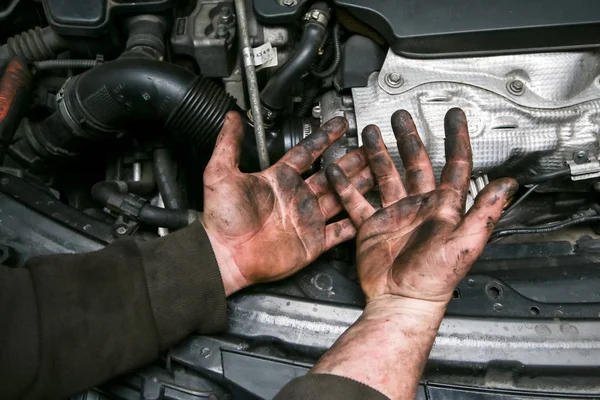 A picture of dirty hands of a guy from the garage above the enigne of a car. Hard and dirty work is behind him.