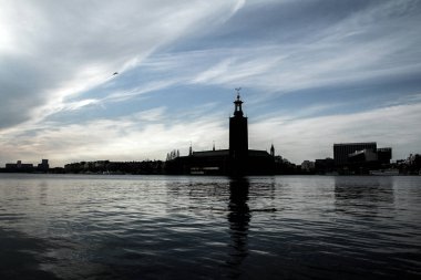 Öğleden sonra güneşine karşı Stockholm belediye binasının silueti. Karanlık bina suya yansıyor.. 