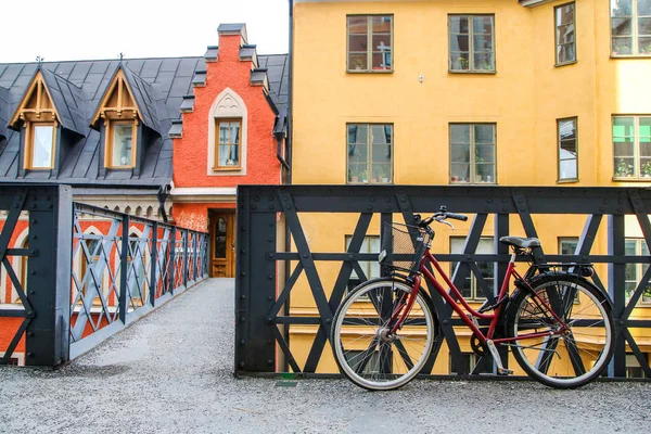 Stockholm 'ün tipik caddesinde köprünün yanında duran yalnız bir kırmızı bisikletin resmi. Motosiklet eski moda gibi görünüyor.