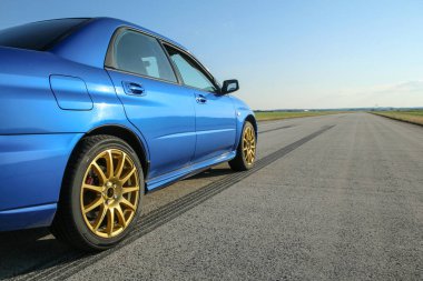 Altın jantlar ile mavi youngtimer spor araba havaalanının beton pist üzerinde duruyor ve hızlı sürücüye hazır. Kalkış yarışının bir parçası olmak gibi. Kauçuk izler görünür. 