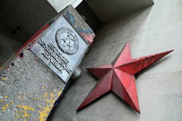 The detail of a border stone in Berlin with the logo of the German democratic republic and a red soviet star on the facade of the house.