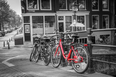 Amsterdam 'daki kanalın üzerindeki köprüde kırmızı bir bisikletin resmi. Arkaplan siyah beyaz.