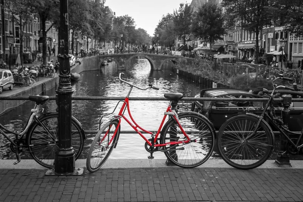 Amsterdam 'daki kanalın üzerindeki köprüde kırmızı bir bisikletin resmi. Arkaplan siyah beyaz.
