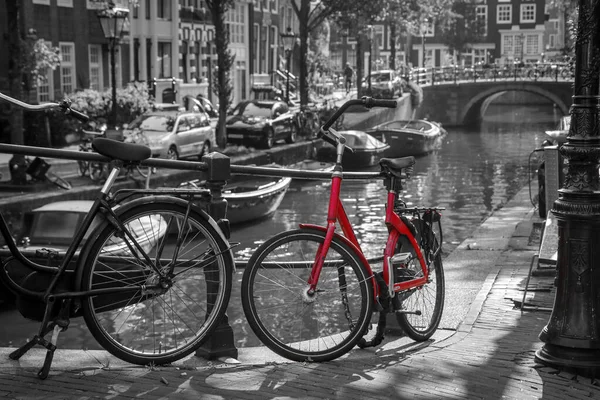 Amsterdam 'daki kanalın üzerindeki köprüde kırmızı bir bisikletin resmi. Arkaplan siyah beyaz.