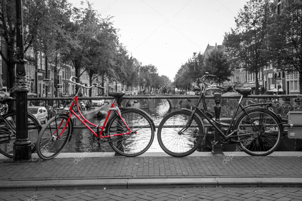 A picture of a red bike on the bridge over the channel in Amsterdam. The background is black and white.