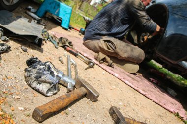 Adam dışarıda arabasını tamir ediyor. Birkaç kirli ekipmanı da var. Kirli ve zor iş..