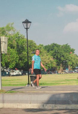 Endonezya, Solo - 21 Eylül 2025: Sağlıklı yaşam tarzı ve spor rutini için parkta yürüyen aktif kıdemli adam, sağlık ve canlılık için temiz hava ve güneşin tadını çıkarıyor