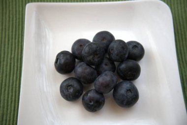 Küçük beyaz bir tabakta servis edilen taze yaban mersinlerinin yakın çekimi..