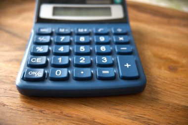 Ahşap bir masanın üzerine yerleştirilmiş mavi hesap makinesinin yakın çekim görüntüsü.