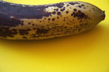 Kahverengi kabuklu bir muzun, fotokopi alanı olan sarı bir arkaplana yakın plan görüntüsü..