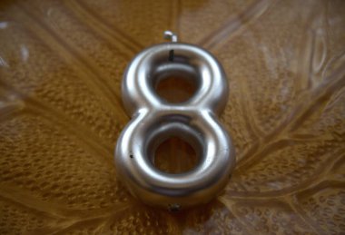 Yaprak desenli bir plakaya yerleştirilmiş 8 numaralı gümüş mum yakın plan..