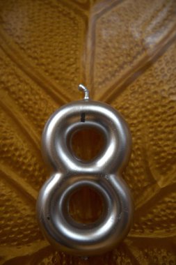 Yaprak desenli bir plakaya yerleştirilmiş 8 numaralı gümüş mum yakın plan..