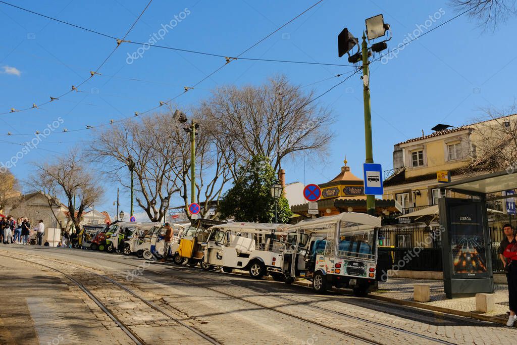 Yellow tram and tuk tuk line on cobblestone street with rails overhead wires and historic buildings sunny day Lisbon Portugal urban transport scene. High quality photo