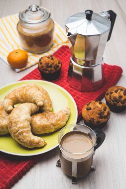 Kahve makinesi, kekler, kruvasan, mandalina ve kahve fincanı
