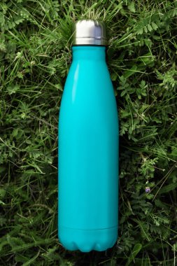 Paslanmaz termos su şişe yeşil çimenlerin üzerinde açık izole. Açık mavi mat renk. Dikey fotoğraf etkisi olmadan