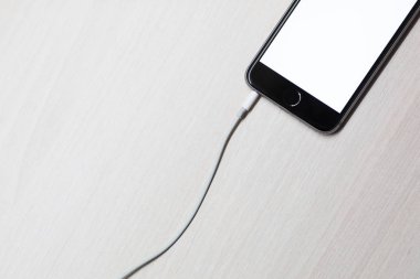 Mockup ekran ve beyaz ahşap masa arka plan üzerinde şarj üzerinden kablo ile Smartphone