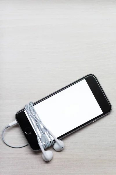 Smartphone com tela de mockup e fones de ouvido na mesa de madeira branca — Fotografia de Stock