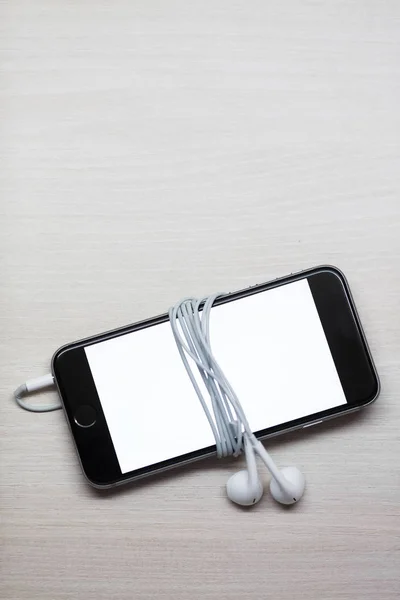 Smartphone com tela de mockup e fones de ouvido na mesa de madeira branca — Fotografia de Stock