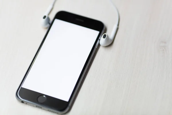 Smartphone con pantalla de maqueta y auriculares en los lados. Fondo de tabla de madera —  Fotos de Stock