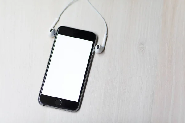 Smartphone com tela de mockup e fones de ouvido nas laterais. Mesa de madeira fundo — Fotografia de Stock