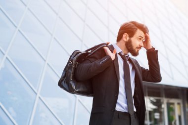 Takım çantası gökdelen windows arka plan üzerinde ciddi hipster sakallı işadamı portresi.