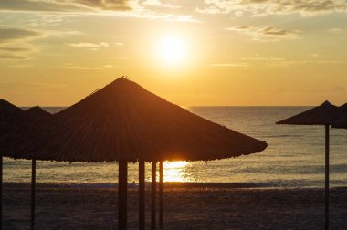 Gündoğumu deniz, plaj şemsiyeleri silüeti.