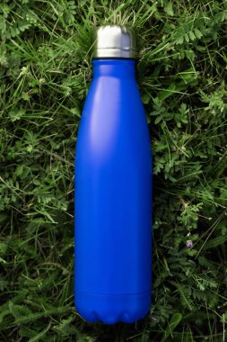 Paslanmaz termos su şişe yeşil çimenlerin üzerinde açık izole. Mavi mat renk. Dikey fotoğraf etkisi olmadan