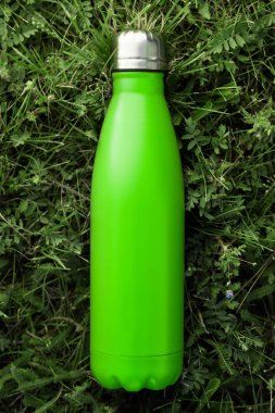 Paslanmaz termos su şişe yeşil çimenlerin üzerinde açık izole. Işık yeşil örtü rengi. Dikey fotoğraf etkisi olmadan