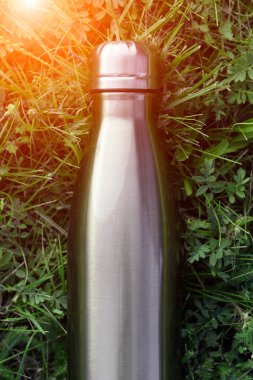 Paslanmaz termos su şişesi, mavi renk. Güneş ışığı etkisi yeşil çim zemin üzerine izole mockup. Parlak alüminyum Vakum termo tumbler şişesi