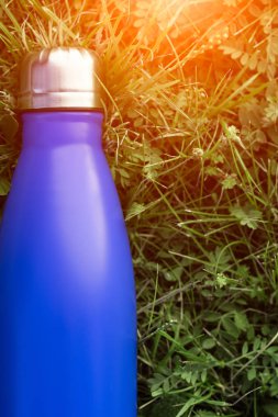 Paslanmaz termos su şişesi, mavi renk. Güneş ışığı etkisi yeşil çim zemin üzerine izole mockup. Parlak alüminyum Vakum termo tumbler şişesi