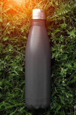 Paslanmaz Termos şişe su, siyah renk için. Güneş ışığı etkisi yeşil çim zemin üzerine izole