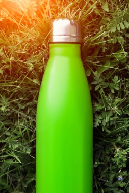 Paslanmaz termos su şişesi, hafif yeşil renk. Güneş ışığı etkisi yeşil çim zemin üzerine izole mockup. Parlak alüminyum Vakum termo tumbler şişesi