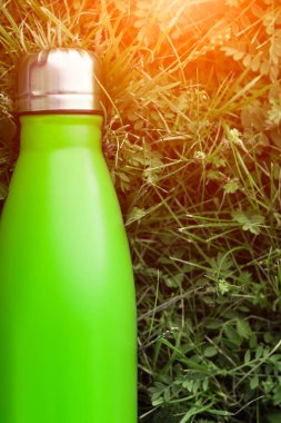 Paslanmaz termos su şişesi, hafif yeşil renk. Güneş ışığı etkisi yeşil çim zemin üzerine izole mockup. Parlak alüminyum Vakum termo tumbler şişesi
