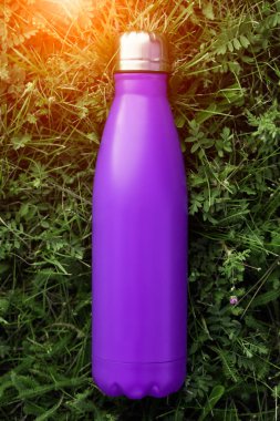 Paslanmaz termos su şişesi, menekşe mor renk. Güneş ışığı etkisi yeşil çim zemin üzerine izole mockup. Parlak alüminyum Vakum termo tumbler şişesi