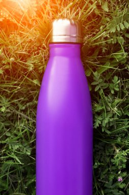 Paslanmaz termos su şişesi, menekşe mor renk. Güneş ışığı etkisi yeşil çim zemin üzerine izole mockup. Parlak alüminyum Vakum termo tumbler şişesi