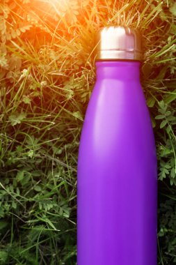 Paslanmaz termos su şişesi, menekşe mor renk. Güneş ışığı etkisi yeşil çim zemin üzerine izole mockup. Parlak alüminyum Vakum termo tumbler şişesi
