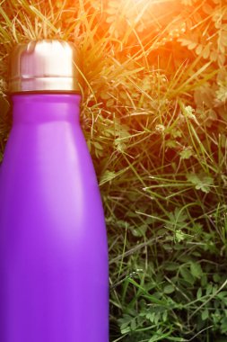 Paslanmaz termos su şişesi, menekşe mor renk. Güneş ışığı etkisi yeşil çim zemin üzerine izole mockup. Parlak alüminyum Vakum termo tumbler şişesi