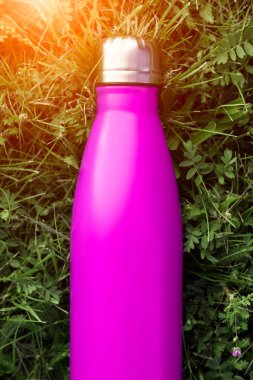 Paslanmaz termos su şişesi, pembe renk. Güneş ışığı etkisi yeşil çim zemin üzerine izole mockup. Parlak alüminyum Vakum termo tumbler şişesi