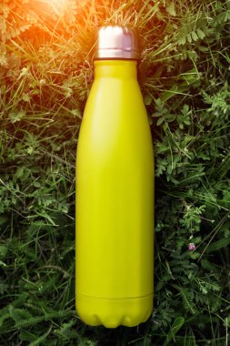 Paslanmaz termos su şişesi, hafif limon rengi. Açık sarı. Güneş ışığı etkisi yeşil çim zemin üzerine izole mockup. Parlak alüminyum Vakum termo tumbler şişesi