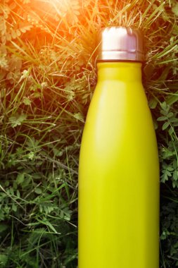 Paslanmaz termos su şişesi, hafif limon rengi. Açık sarı. Güneş ışığı etkisi yeşil çim zemin üzerine izole mockup. Parlak alüminyum Vakum termo tumbler şişesi