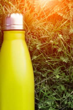 Paslanmaz termos su şişesi, hafif limon rengi. Açık sarı. Güneş ışığı etkisi yeşil çim zemin üzerine izole mockup. Parlak alüminyum Vakum termo tumbler şişesi