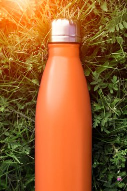 Paslanmaz termos su şişesi, portakal rengi. Güneş ışığı etkisi yeşil çim zemin üzerine izole mockup. Parlak alüminyum Vakum termo tumbler şişesi
