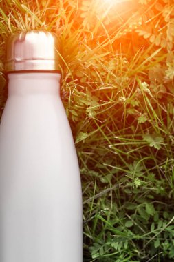 Paslanmaz termos su şişesi, beyaz renk. Güneş ışığı etkisi yeşil çim zemin üzerine izole mockup. Parlak alüminyum Vakum termo beyaz diş şişesi